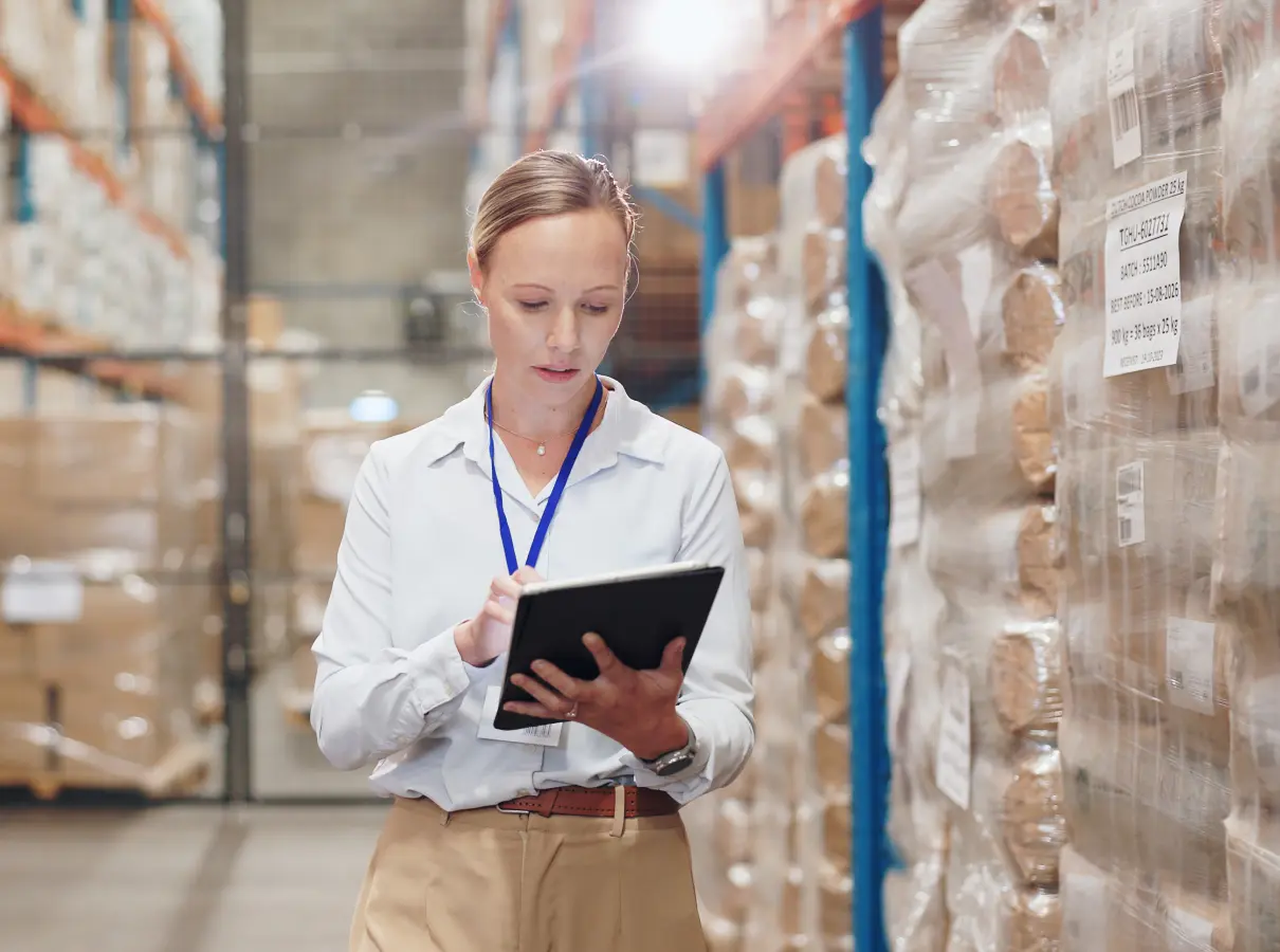 A woman using a tablet in a warehouse aisle.