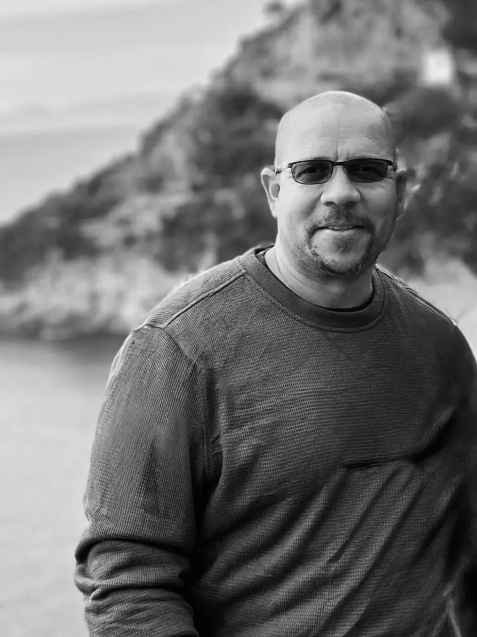 A man wearing sunglasses and a sweater, smiling outdoors.
