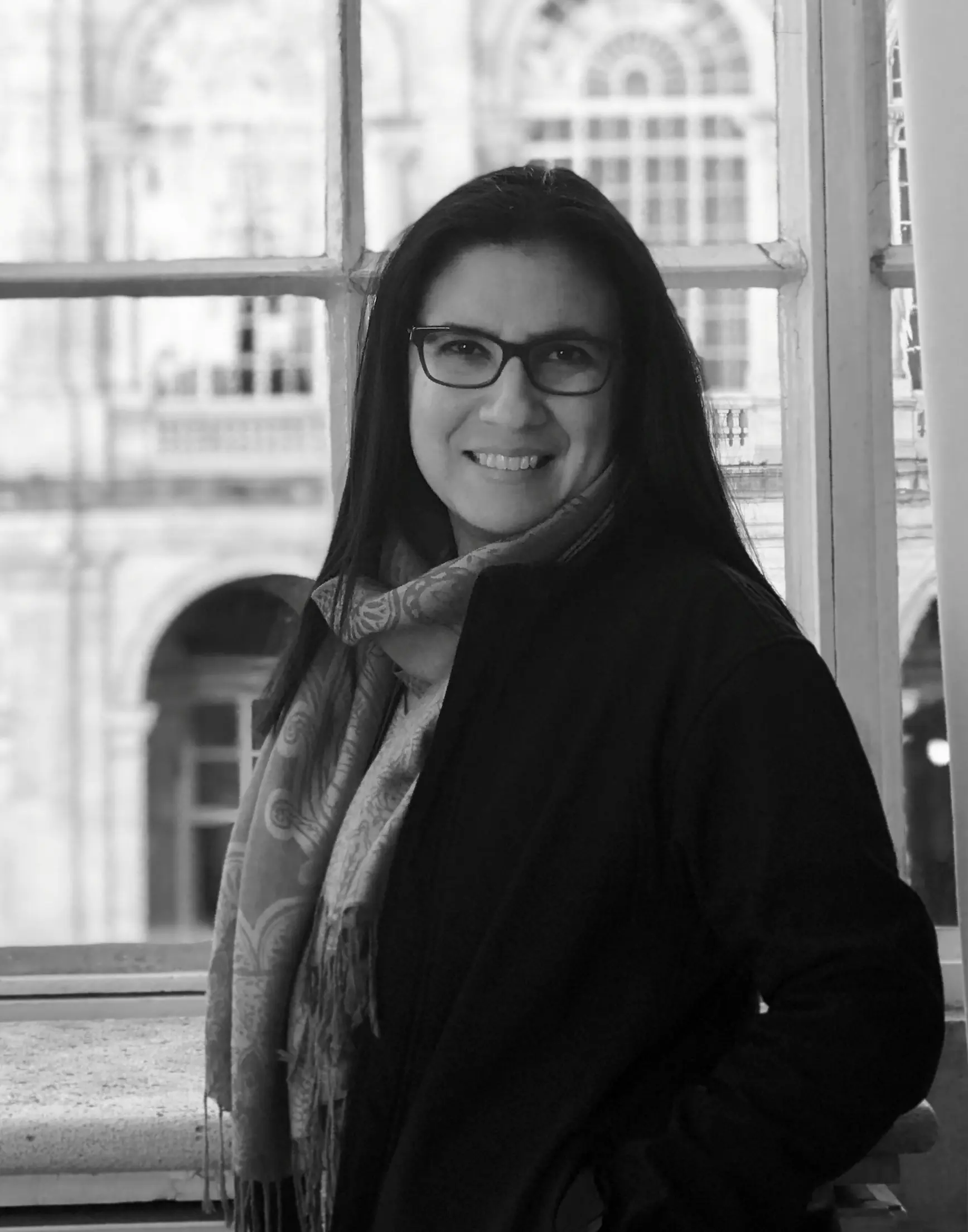 Black and white portrait of a smiling woman with glasses and a scarf.